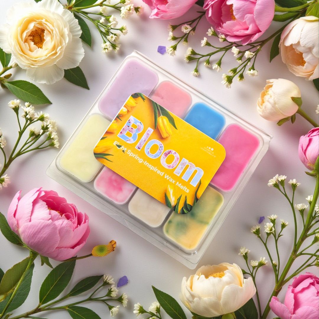 Set of colourful wax melts in a clear container with 'Bloom' branding, surrounded by flowers on a light background.