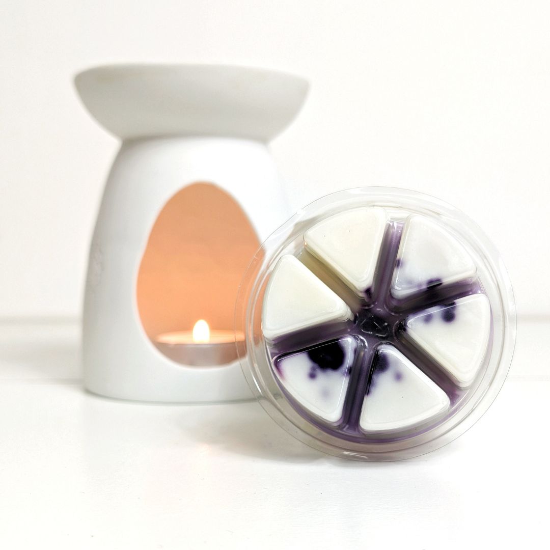 White wax warmer with a lit candle and a wheel of wax melts on a white background