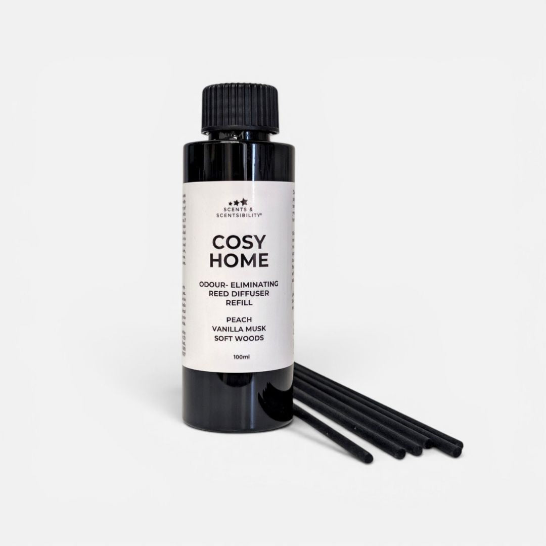 A black bottle of Cosy Home odour-eliminating Reed Diffuser Refill with a white label, shown next to several black reeds on a light gray background.