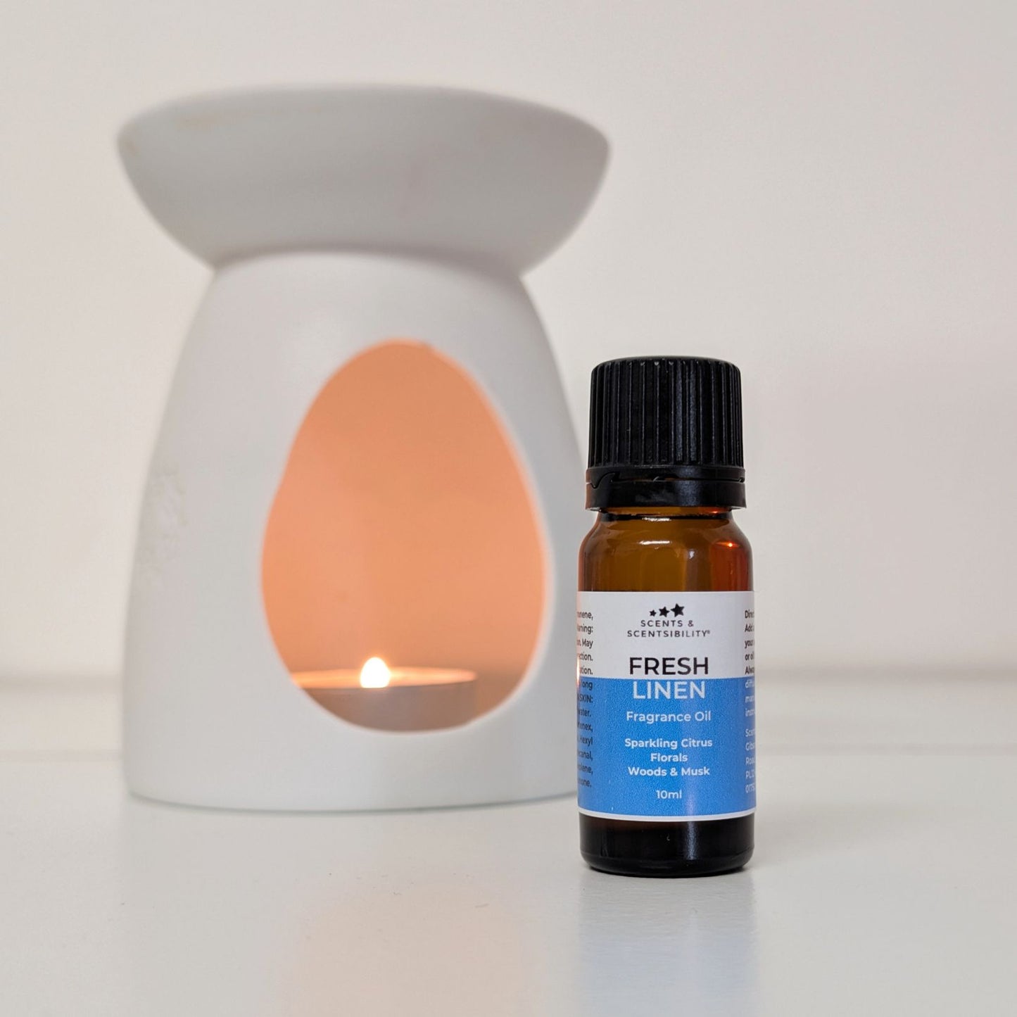 Fragrance oil bottle labeled 'Fresh Linen' next to a ceramic warmer with a lit candle.