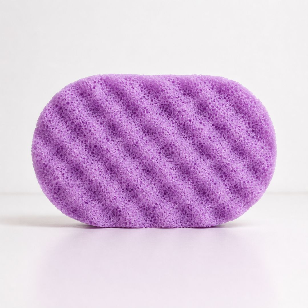 A purple oval-shaped textured sponge with soap, shown on a clean white background.