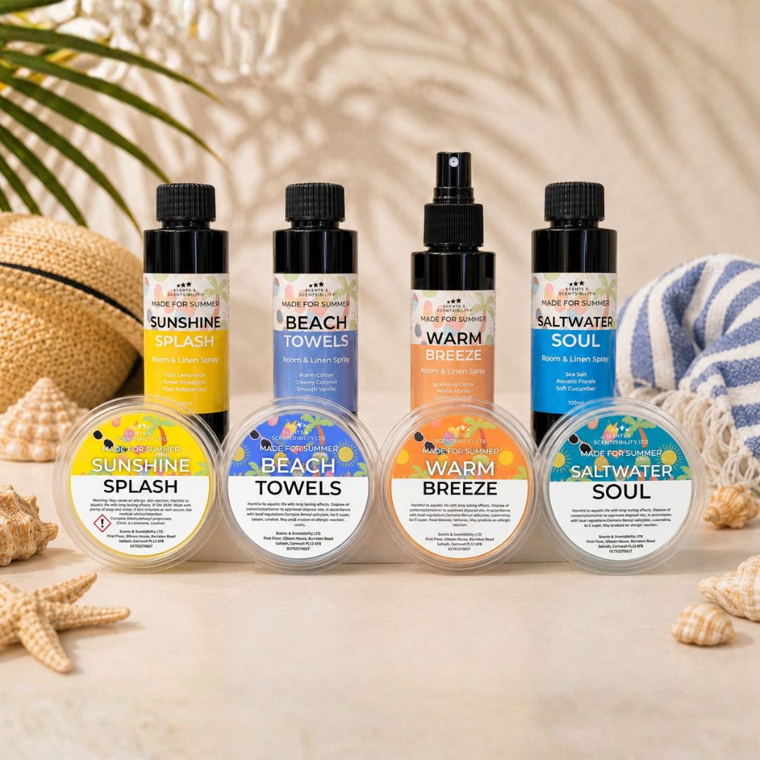 A set of four scented products arranged on a light beige surface with beach-themed props: two spray bottles labeled Sunshine and Warm Breeze, two pump bottles labeled Beach Towels and Saltwater Soul, and four round wax melt tubs labeled Sunshine Splash, Beach Towels, Warm Breeze, and Saltwater Soul. The scene includes a straw hat, starfish, shells, and a blue-and-white towel.