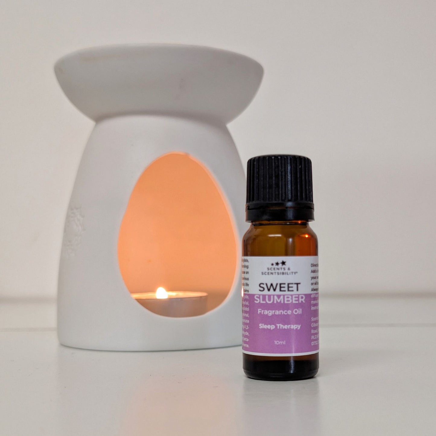 Fragrance oil bottle labeled 'Sweet Slumber' next to a lit wax warmer on a white background