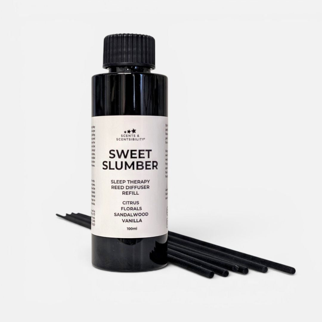 A black plastic bottle of Sleep Therapy 'Sweet Slumber' sleep therapy reed diffuser refill, with several black reed diffuser sticks laid out on a light gray background.