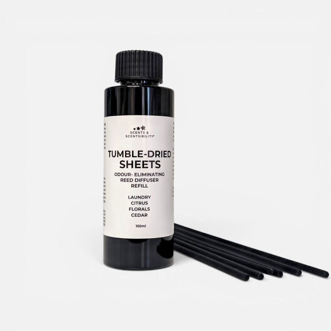 A black bottle of 'Tumble Dried Sheets' scent-eliminating Reed Diffuser Refill by Scents & Scentsibility, shown with six black reeds on a clean white background.