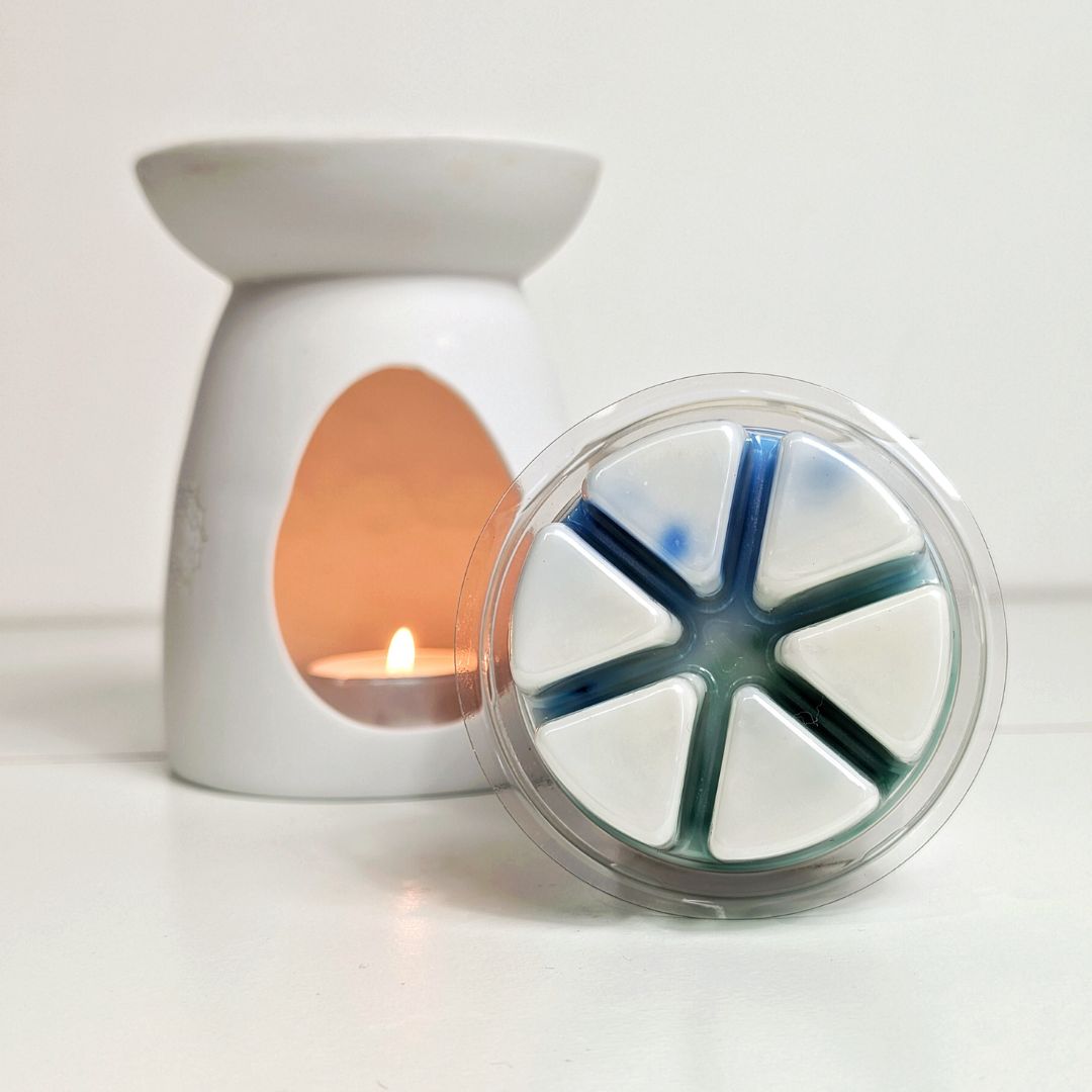 A wax melter with a lit candle inside and a clear container with wax melts on a white background.
