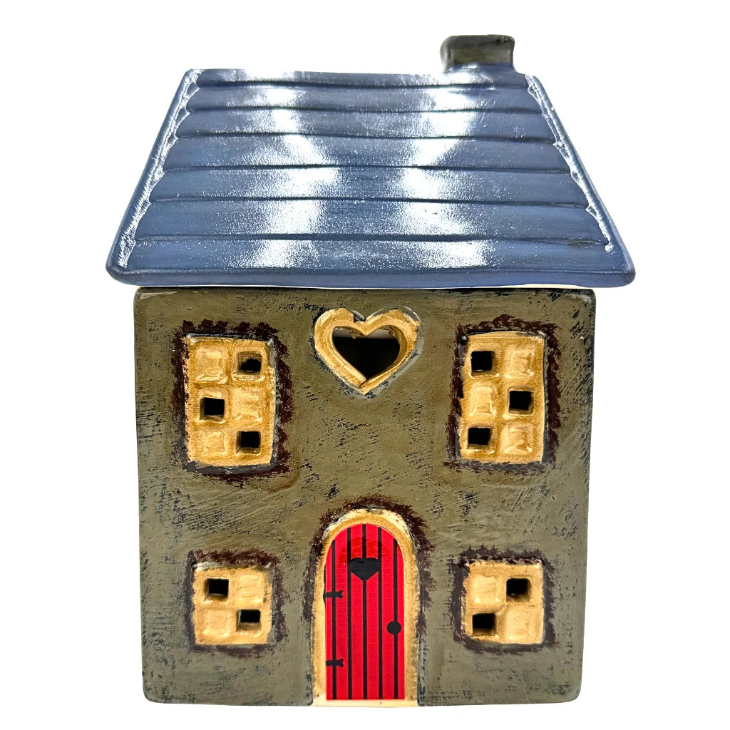 A ceramic cottage house wax melt warmer with a textured gray-brown body, a dark blue-gray roof, a bright red door, and gold-colored window and heart-shaped trim details, isolated on a white background.