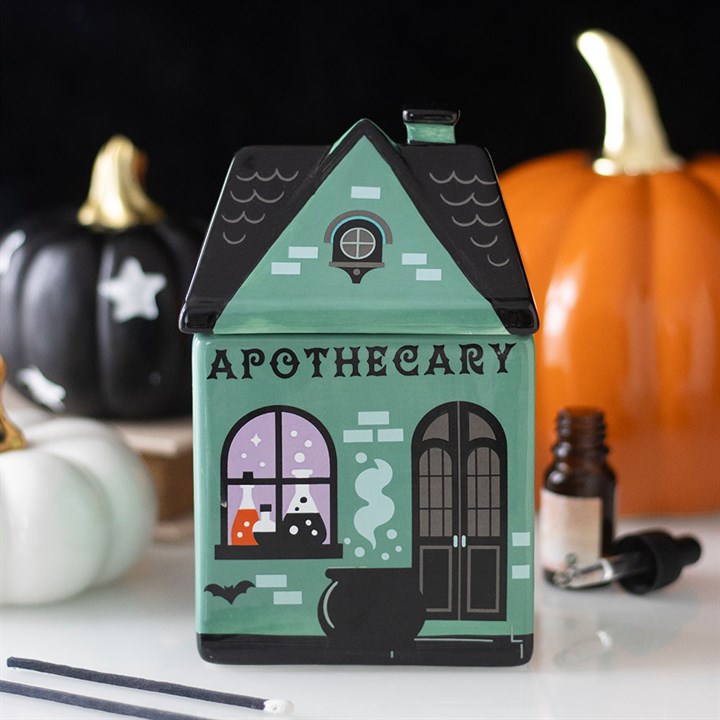 Green apothecary house-shaped wax melt & oil burner with pumpkins and bottles in the background