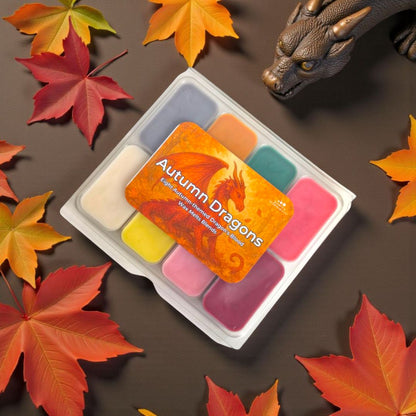 Set of wax melts with 'Autumn Dragons' packaging surrounded by autumn leaves on a brown background