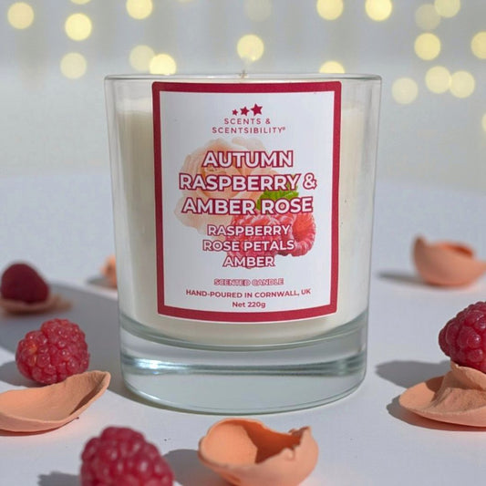 Candle with 'Scents & Scentsibility' label featuring autumn raspberry and amber rose, surrounded by raspberries and petals.