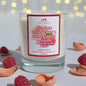 Candle with 'Scents & Scentsibility' label featuring autumn raspberry and amber rose, surrounded by raspberries and petals.