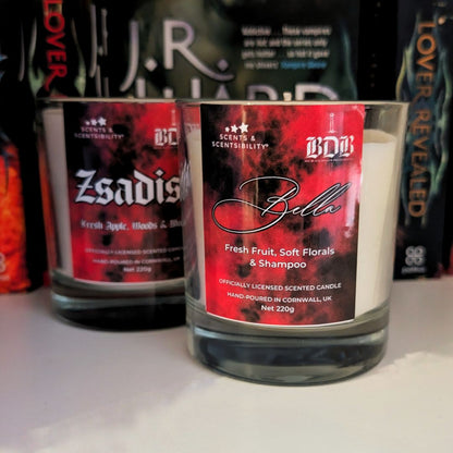 Scented candle labeled 'Bella' with a red label featuring text, in front of other branded candles.