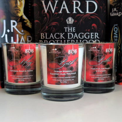 Three candles with red labels in front of a book titled 'The Black Dagger Brotherhood' by J.R. Ward.