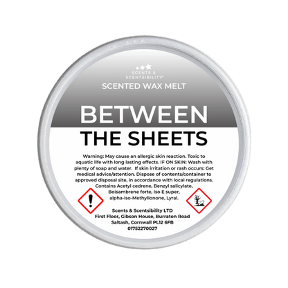 Scented wax melt container labeled 'Between the Sheets' with warning information on a green background