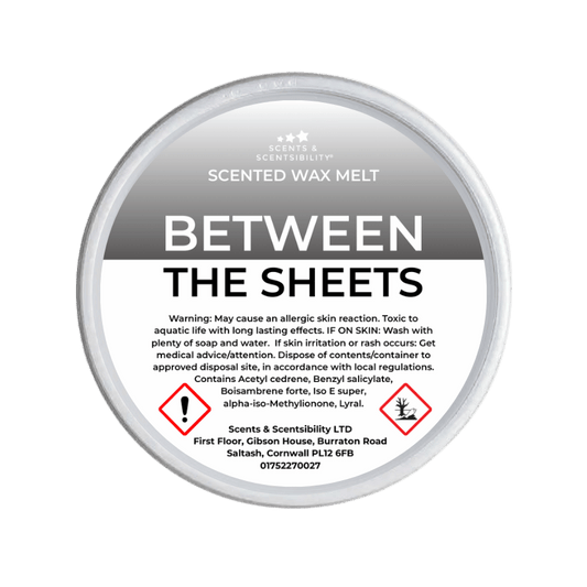 Scented wax melt container labeled 'Between the Sheets' with warning information on a green background