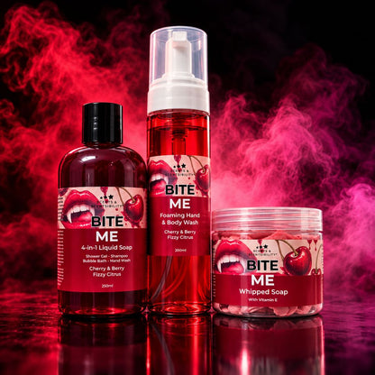 Three BITE ME haircare products in a studio setup with dramatic red and pink smoke: a liquid soap bottle, a foaming hand and body wash pump bottle, and a whipped soap jar, all with cherry-and-lips labels.