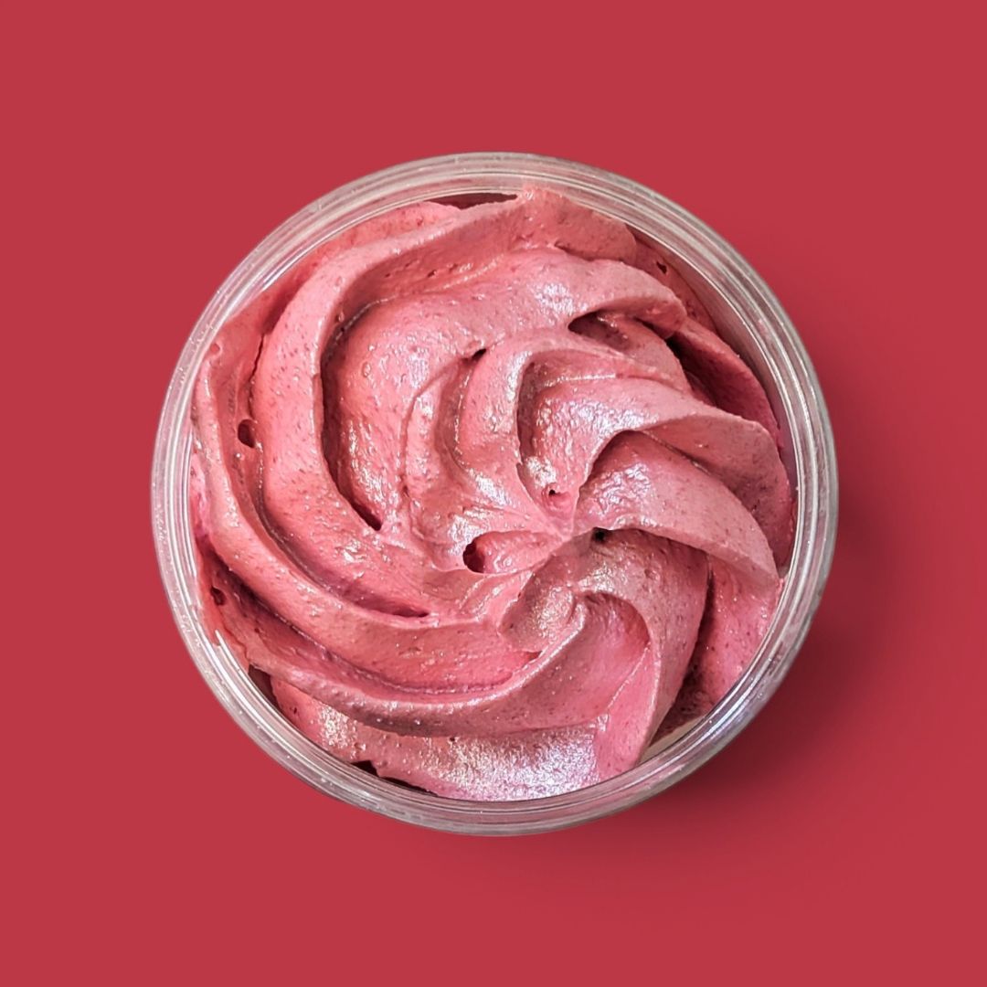 A top-down view of a clear round container filled with dark pink, shimmery whipped soap, swirled in a spiral pattern, set against a solid red background.