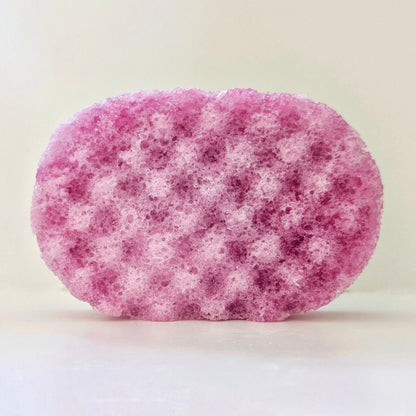 A pink and white textured bath sponge with a porous, bubbly surface, photographed on a plain off-white background.