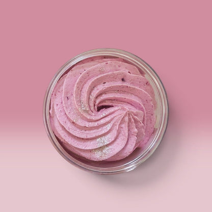 Pink whipped soap swirled in a clear container, photographed from above on a soft pink background.