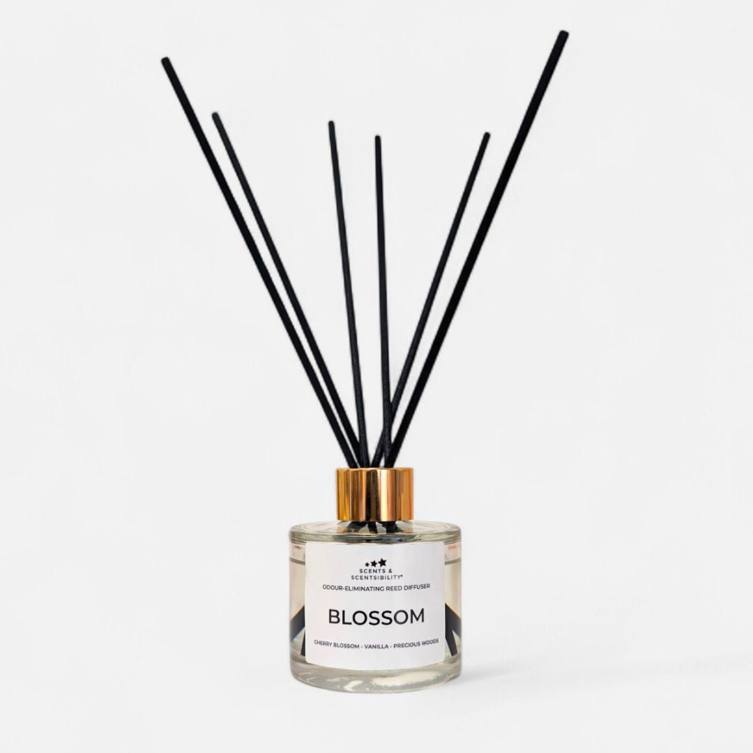 A glass bottle with clear liquid, gold collar and black fibre reeds with a white label