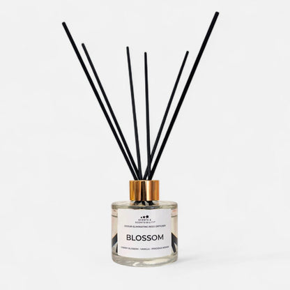 A glass bottle with clear liquid, gold collar and black fibre reeds with a white label