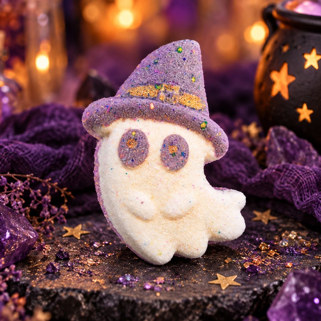 Boo Witch ghost-shaped bath bomb with a grey-purple witch hat and purple eyes, styled with amethyst crystals, purple fabric and glowing Halloween décor.