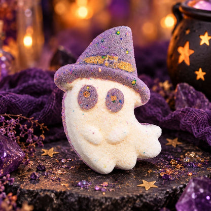 Boo Witch ghost-shaped bath bomb with a grey-purple witch hat and purple eyes, styled with amethyst crystals, purple fabric and glowing Halloween décor.