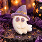 Boo Witch ghost-shaped bath bomb with a grey-purple witch hat and purple eyes, styled with amethyst crystals, purple fabric and glowing Halloween décor.