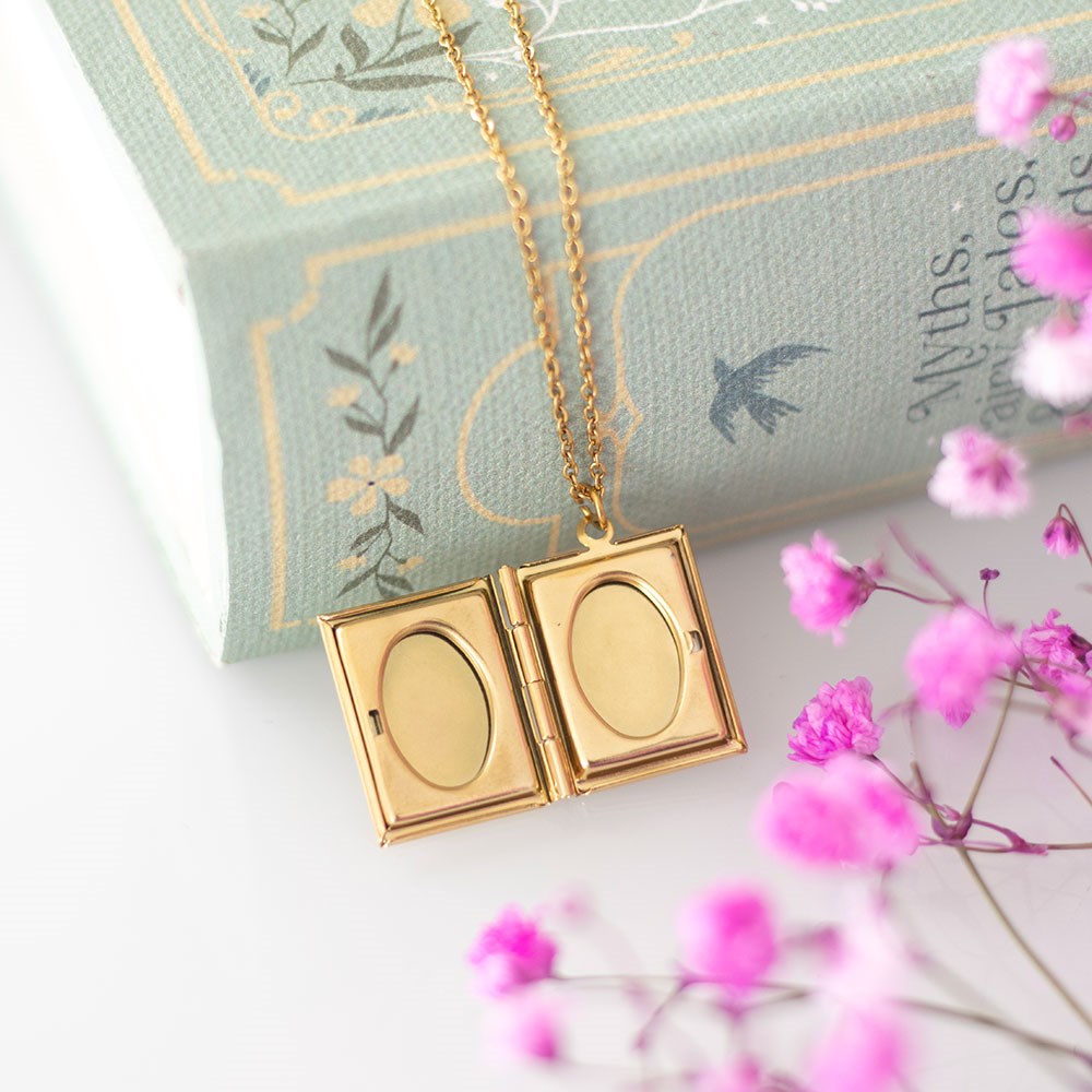 Gold necklace with a double locket on a decorative pillow with pink flowers.