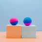 Two colorful bath bombs on geometric blocks with a light blue background