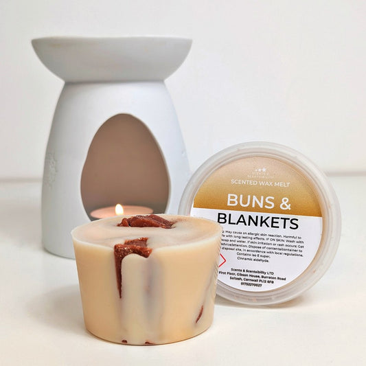 Scented wax melt container labeled 'Buns & Blankets' with a lit wax melt burner on a white background