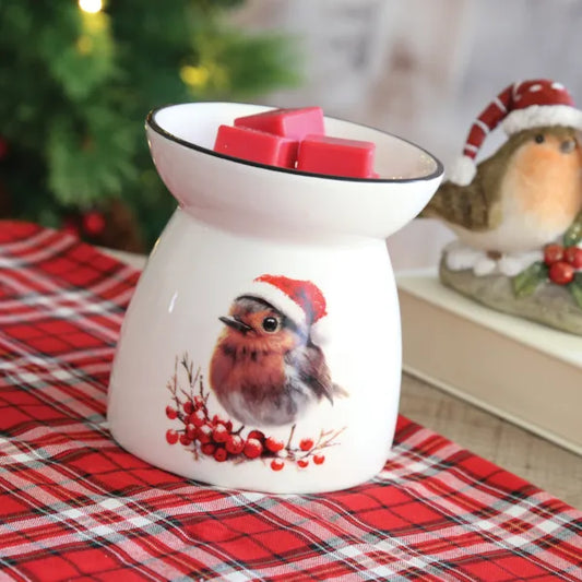 A white wax melt and oil burner with a picture of a robin wearing a Christmas hat on a cosy surface. 