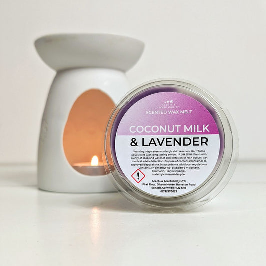Scented wax melt container labeled 'Coconut Milk & Lavender' with a lit candle in the background.