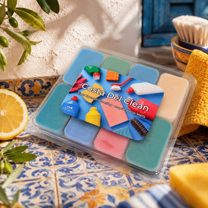 A clear plastic clamshell package of Costa Del Clean multi-color wax melts sits on a blue and yellow patterned tile surface. The package contains multiple square wax melts in shades of blue, green, pink, and beige, with a colorful label showing cleaning-themed illustrations and the text 'Costa Del Clean'.