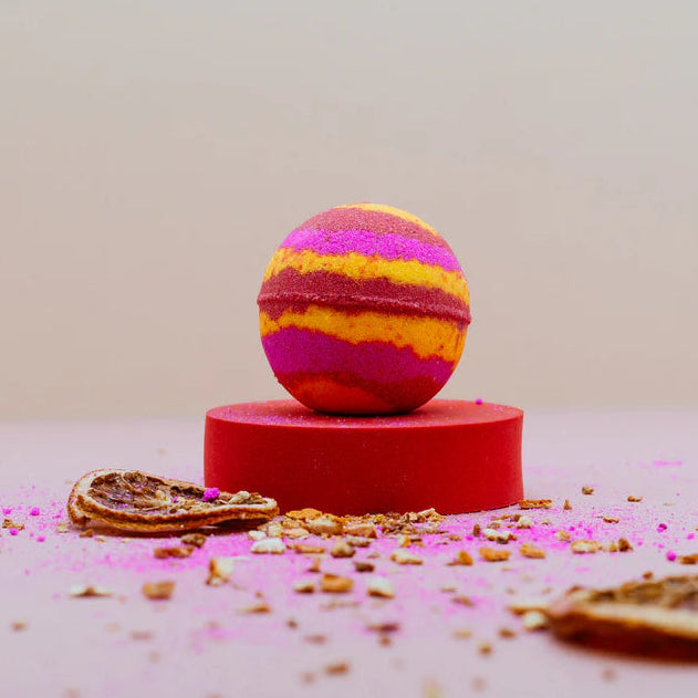 A Pink, yellow and red bath bomb surrounded by dried citrus