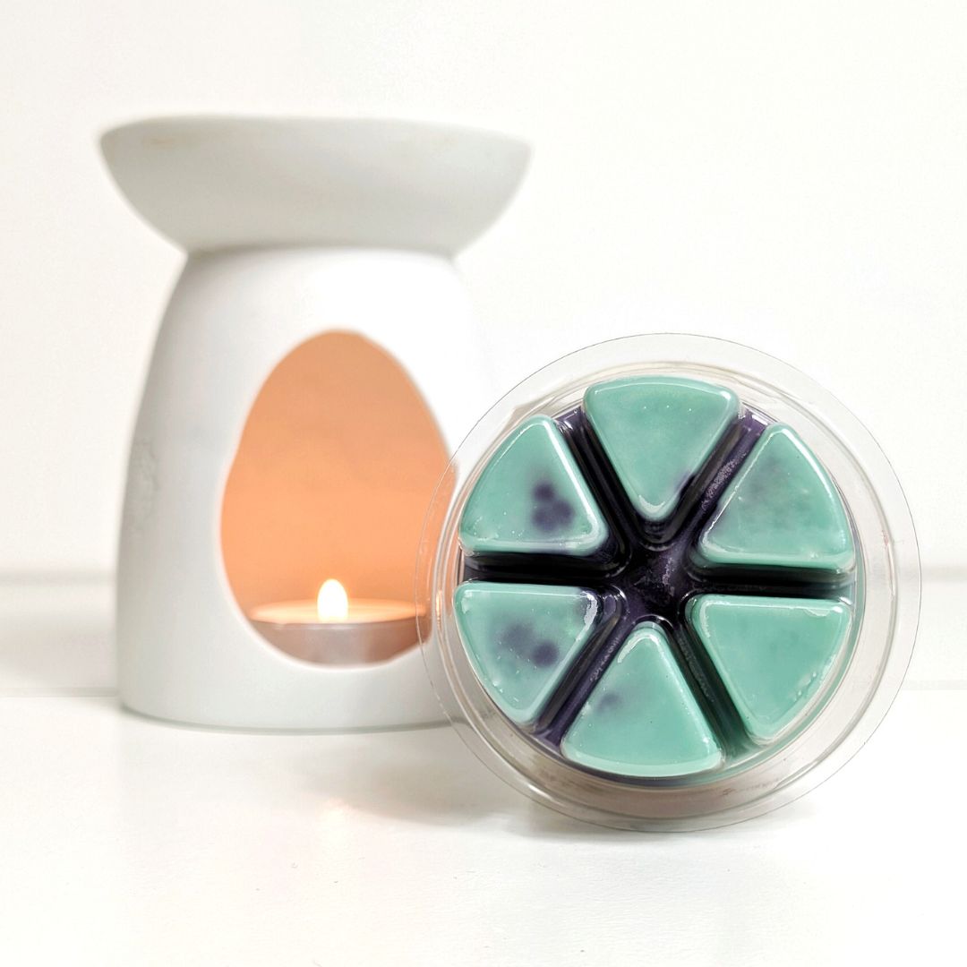 White wax warmer with a lit candle and a container of teal wax melts on a white background