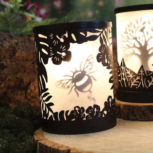 A black wax melt warmer with glowing light and bumble bee silhouette design on a wooden shelf. 