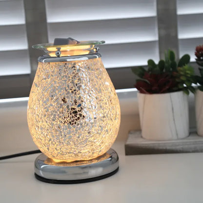 Jupiter Mosaic Electric Wax Melt Burner illuminated with a warm golden glow, highlighting its sparkling silver mosaic glass design on a tabletop in a cosy home setting.
