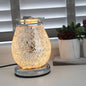 Jupiter Mosaic Electric Wax Melt Burner illuminated with a warm golden glow, highlighting its sparkling silver mosaic glass design on a tabletop in a cosy home setting.