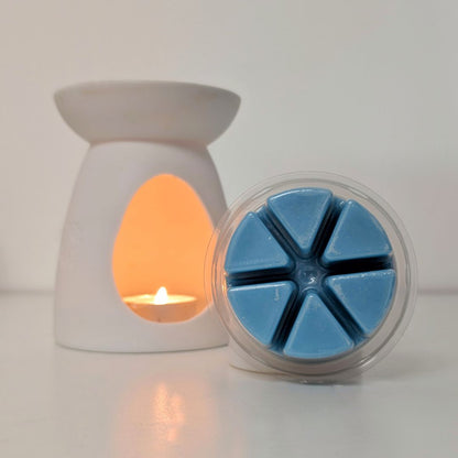 White wax warmer with a lit candle and a container of blue wax melts on a white background