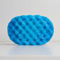 A blue, textured sponge, filled with soap on a white background.