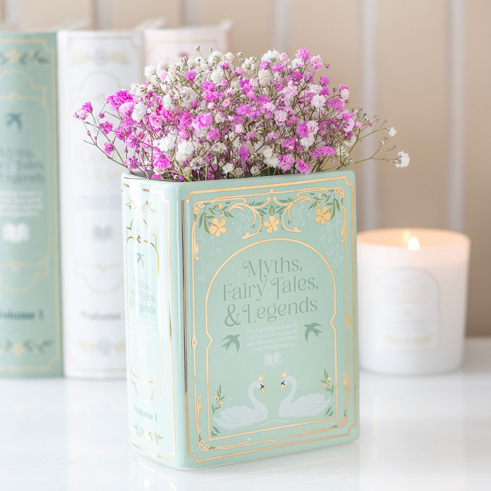 Decorative book shaped vase with flowers on a table with candles in the background