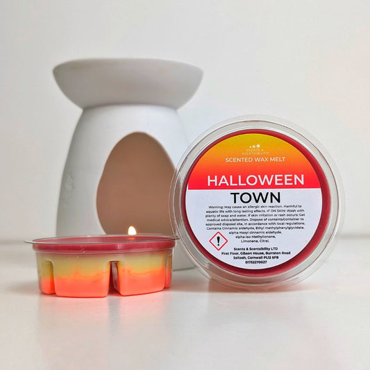 Scented wax melt container labeled 'Halloween Town' with a lit wax melt  burner beside it on a white background.