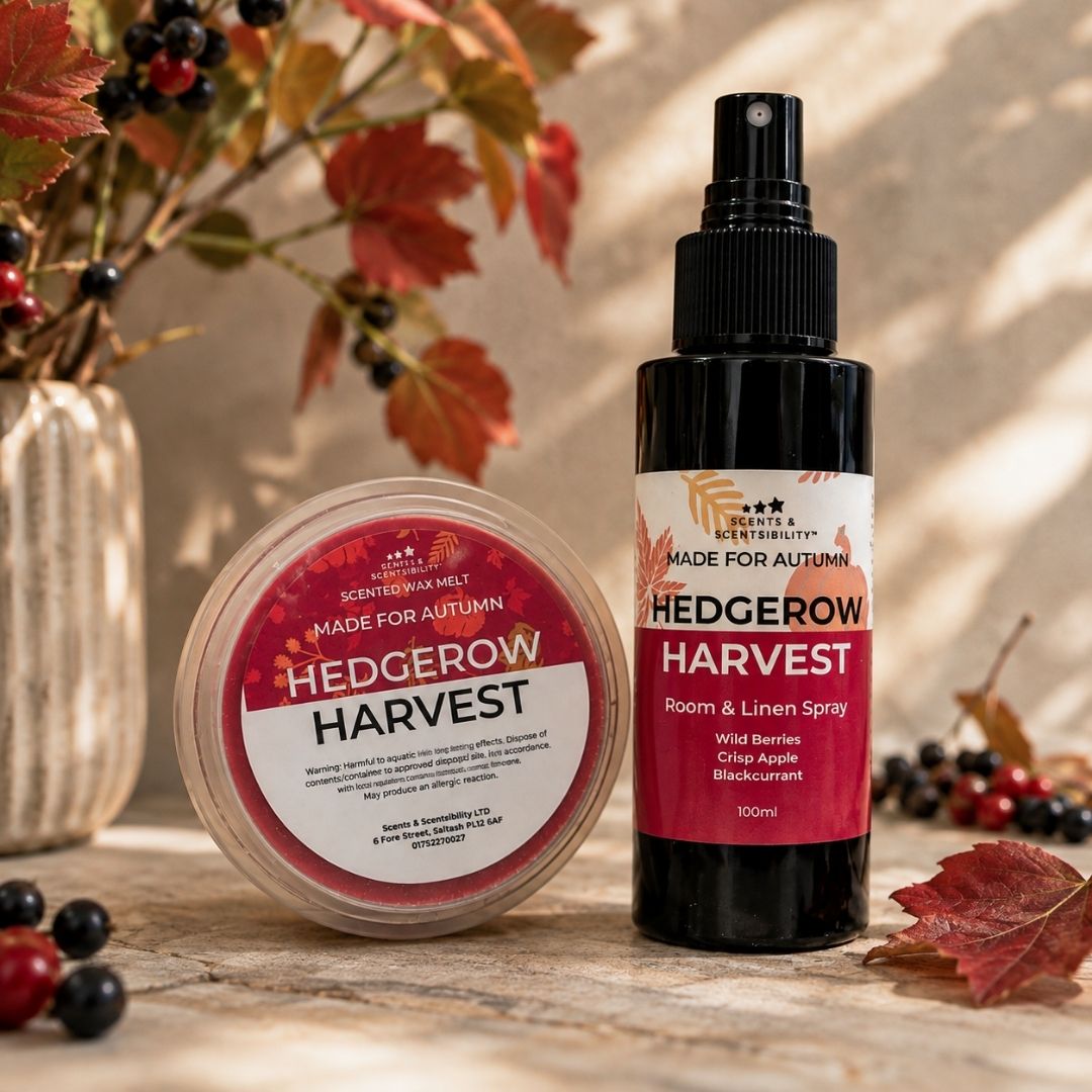 A bottle of Hedgerow Harvest Room and Linen Spray and a round tin of Hedgerow Harvest Scented Wax Melts on a rustic wooden surface with autumn leaves and berries.
