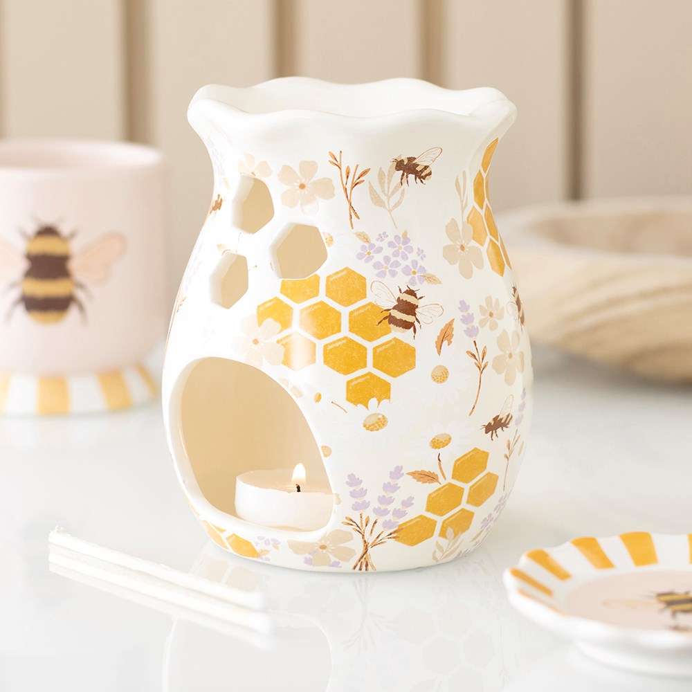 Honey Bee Fluted Wax Warmer & Oil Burner displayed with a lit tealight, surrounded by matching bee-themed accessories, showing its golden honeycomb and floral design.