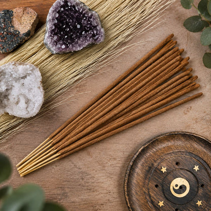 A set of incense sticks arranged on a wooden surface with dried grass, crystals, and a round wooden holder with a gold moon and star symbol.