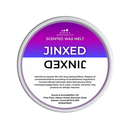 A Jinxed Scented Wax Melt by Scents & Scentsibility, featuring a purple-to-white gradient label with bold white text, shown against a solid dark green background.