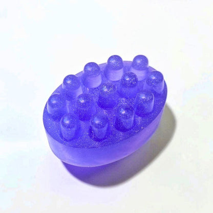 Purple oval massage soap bar with raised textured bumps on a white background.