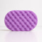 A purple oval-shaped textured sponge with soap, shown on a clean white background.
