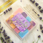 A selection box of colourful wax melts on a white surface with lavender flowers. 